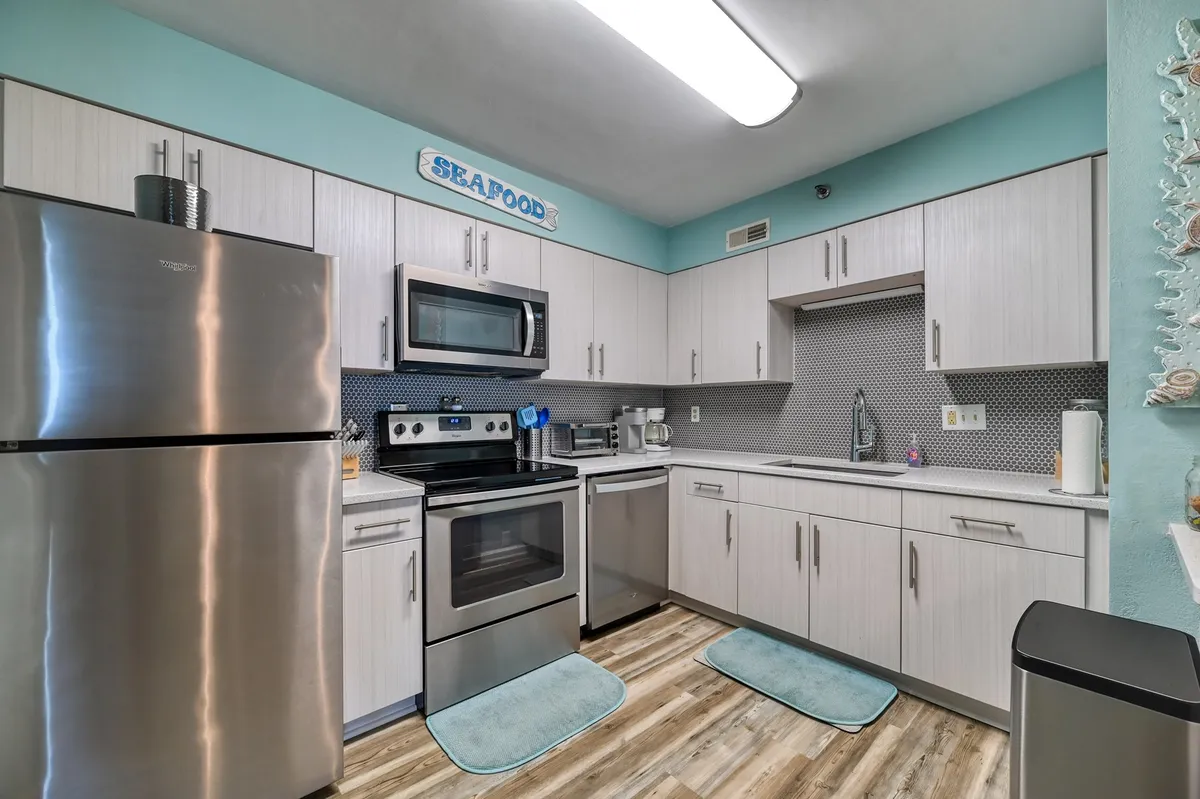 A modern kitchen with stainless steel appliances, a blue accent wall, contemporary cabinetry, and cozy rugs underfoot. The scene highlights the kitchen’s functionality and cheerful ambiance, emphasizing the space’s suitability for cooking and casual dining.