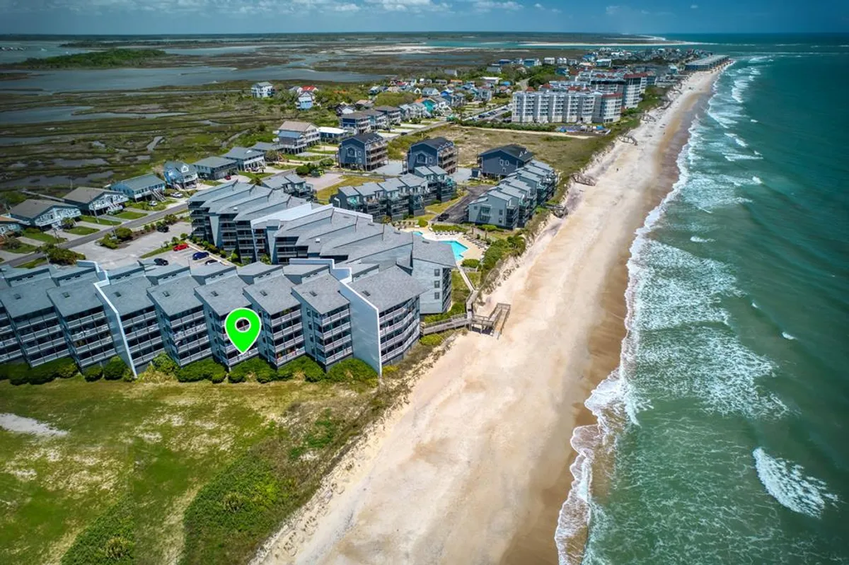 A sweeping exterior view captures the resort's beachfront, with sun-drenched sand leading to gentle ocean waves. Residential buildings stand in the background, seamlessly blending the private condo setting with the expansive coastal landscape.