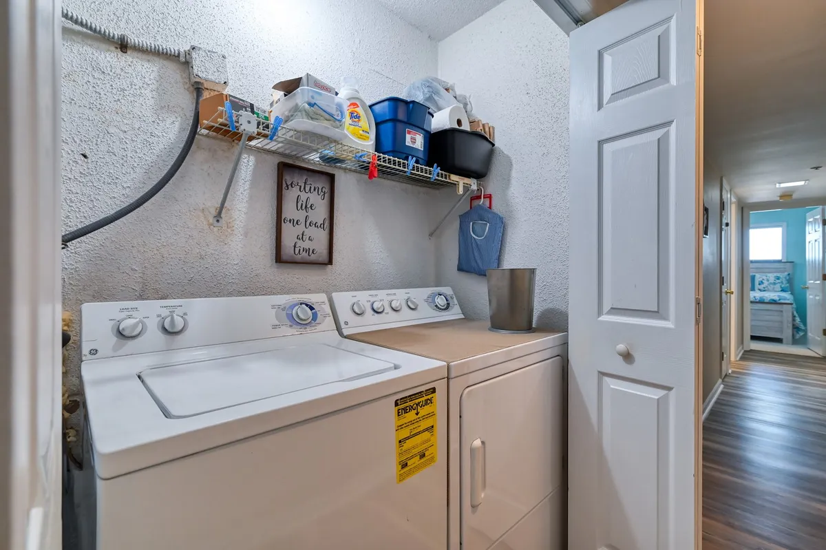 A fully equipped laundry area with a washing machine, dryer, neatly arranged supplies, and a welcoming decorative sign. The space is organized and user-friendly, ensuring guests’ practical needs are well met.