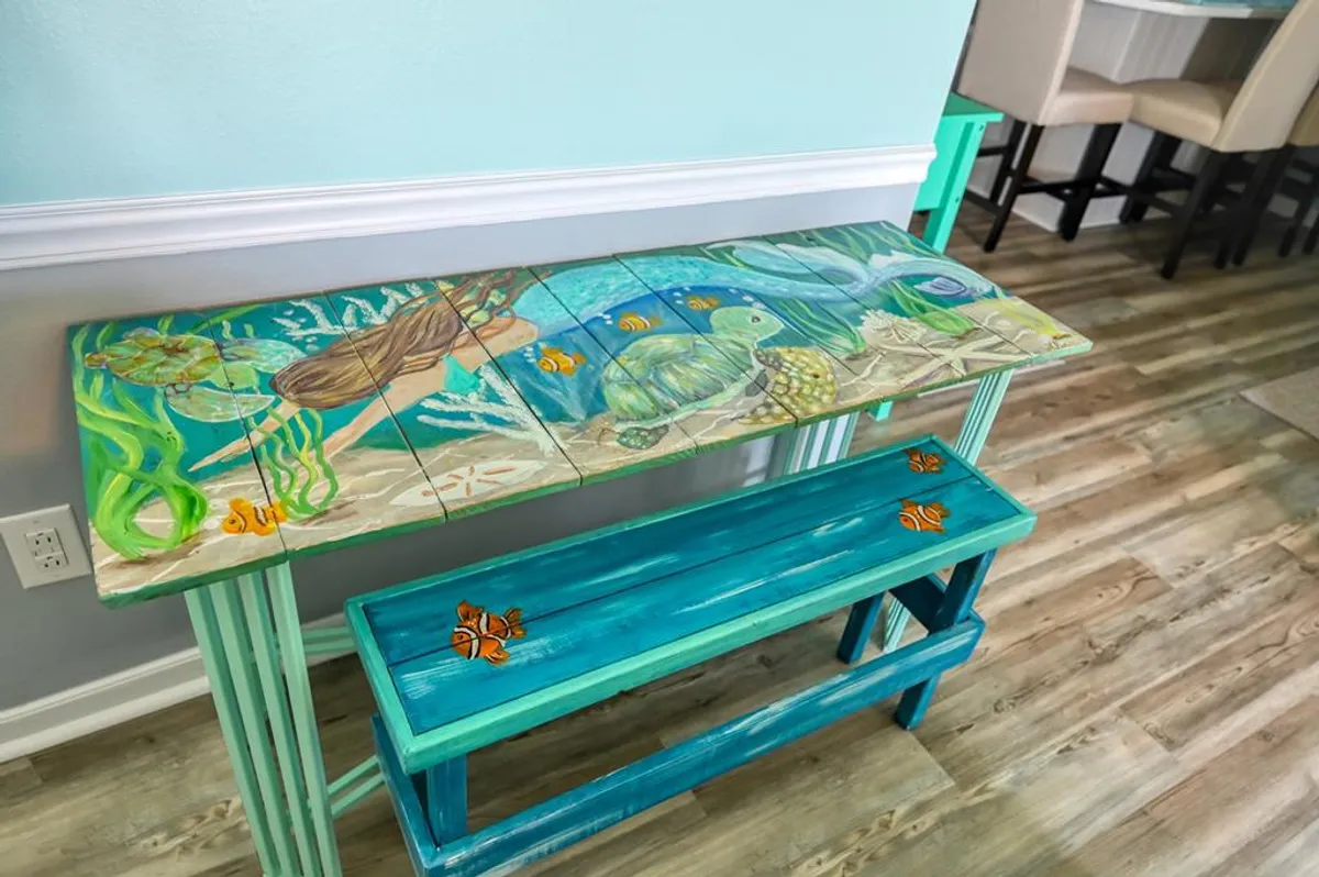 A colorful dining table with marine-themed artwork and decorative stools creates a joyful and inviting setting. The table’s design is playful and artistic, making it especially appealing for children or family gatherings.