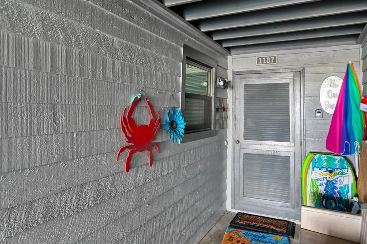 A cheerful entryway features vibrant coastal decor—like a red crab and blue flower decoration—with colorful beach towels and a doormat, evoking a welcoming and beach-ready vibe.